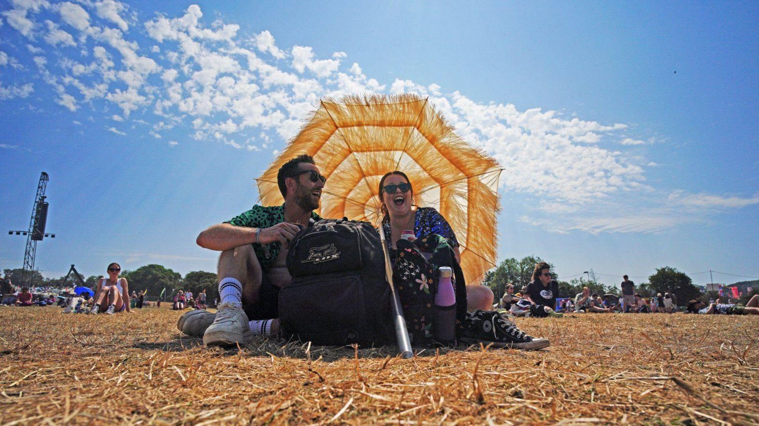 A couple sit under an umbrella under a sunny sky