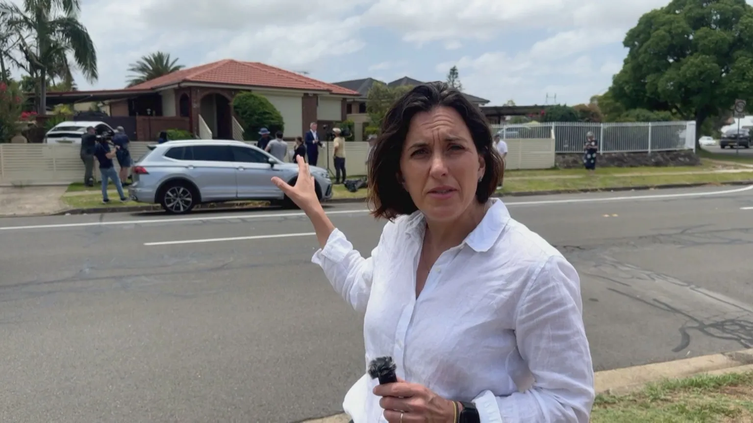Katy Watson stands outside a house with a car parked outside of it.