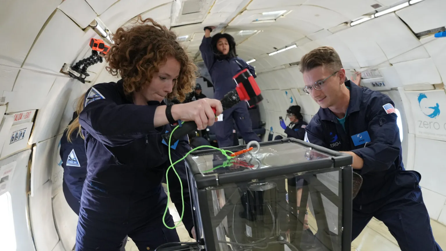 Steve Boxall Two young researchers in blue jump suits work on some equipment on a low-gravity flight.