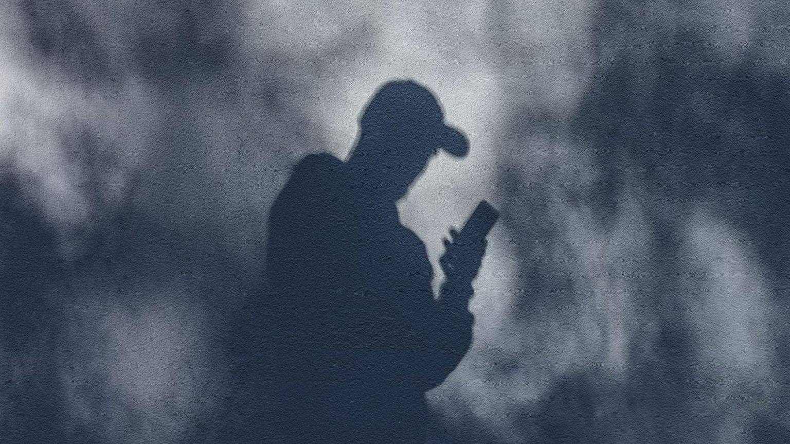 Shadow of a man in a baseball cap holding a phone