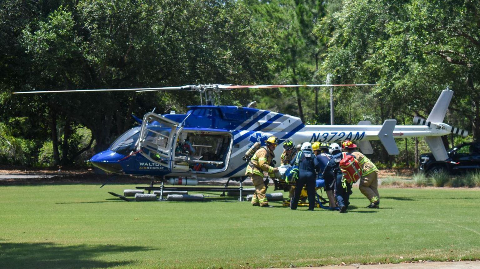 A crowd of people taking someone towards a rescue helicopter which has landed on grass