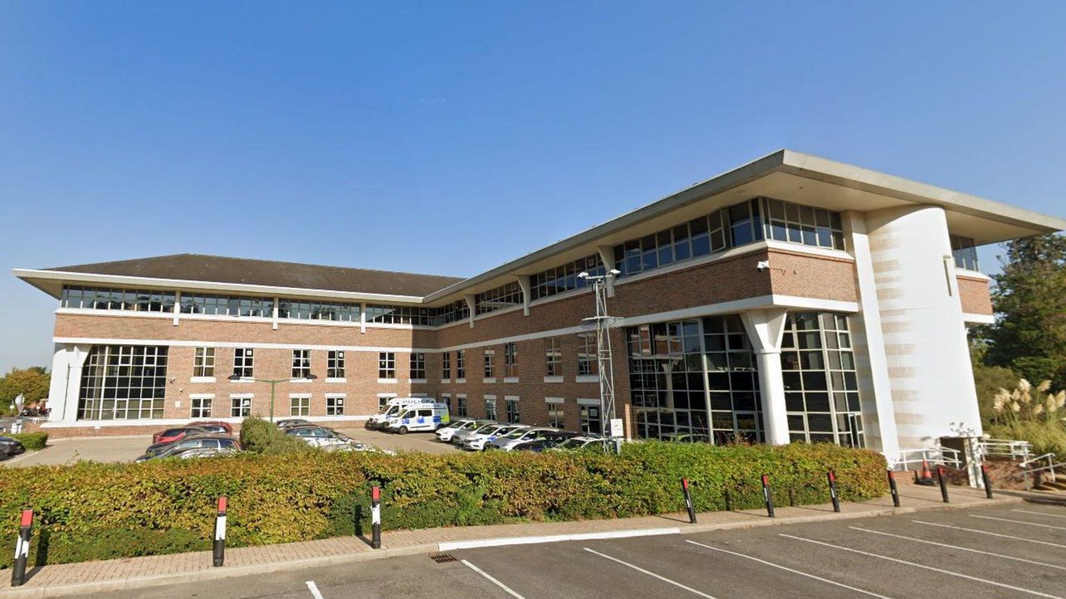 The outside of The Civic Centre in Esher which is a three storey brick building with large glass windows and a car park in front of it