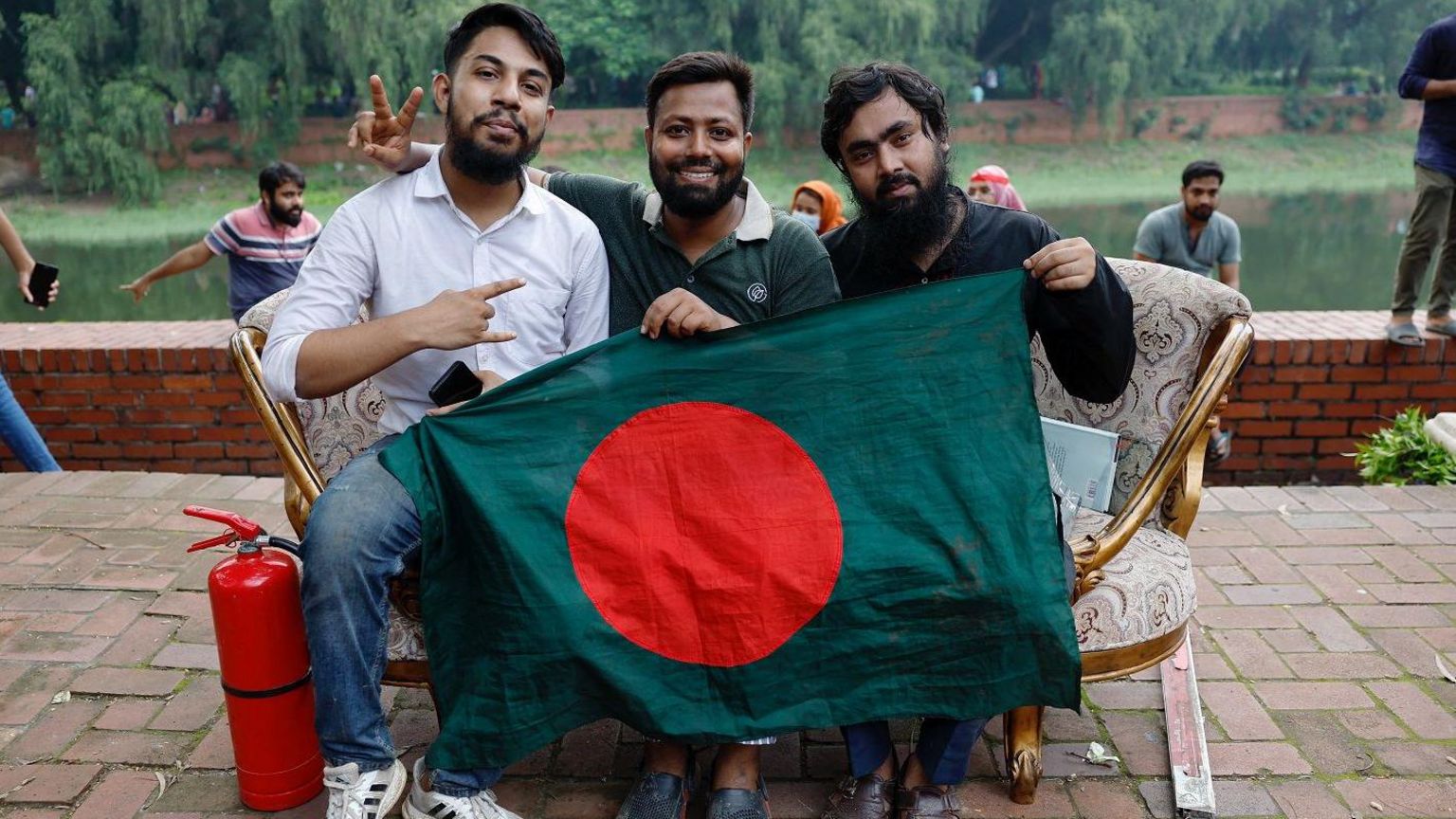 People pose for a picture with the flag of Bangladesh as they sit on a sofa looted from the Ganabhaban, the Prime Minister's residence, after the resignation of PM Sheikh Hasina in Dhaka, Bangladesh, August 5, 2024.