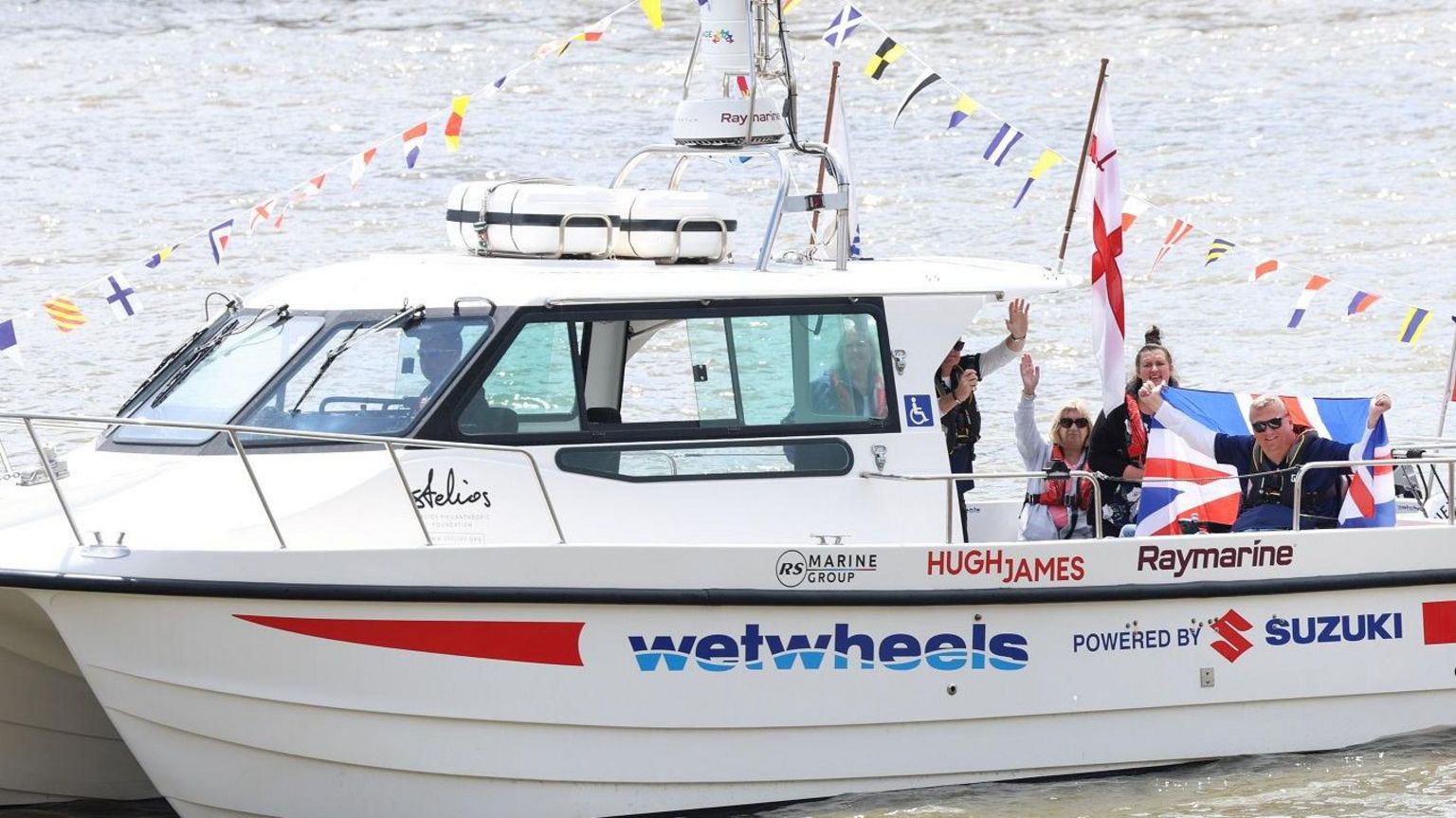 A boat decorated with flags and bunting, with Mr Holt holding up a flag on the back of it