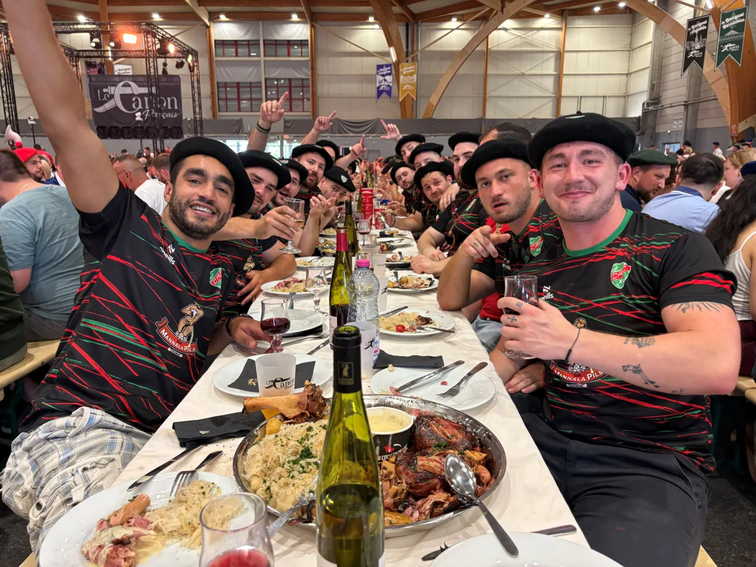 BBC A group of young men wearing matching sports tops and black berets sit at a long table with platters of food and wine