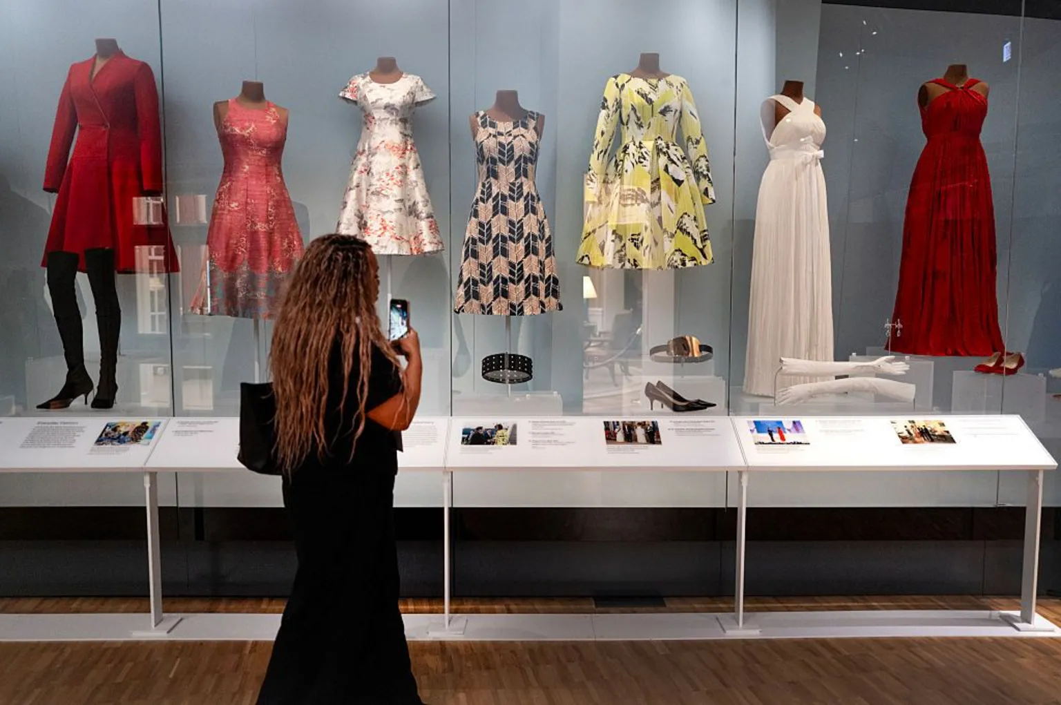 Scott Olson/Getty Images A woman views a selection of dresses worn by Michelle Obama while she was first lady. The dresses are patterned and displayed on mannequins, accompanied by the shoes and other