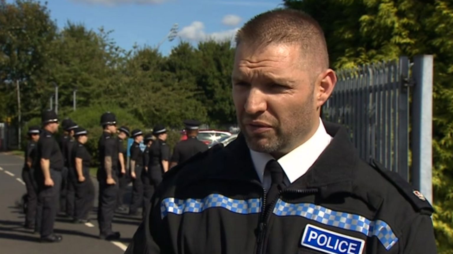 Superintendent Gareth Mason in his police uniform standing in a street with a number of police officers stood at attention behind him