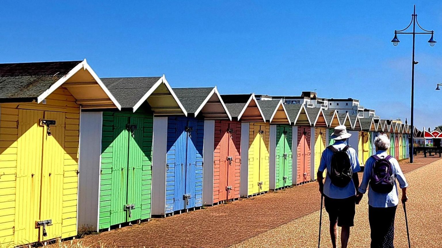 A couple walking along colourful huts on the beach
