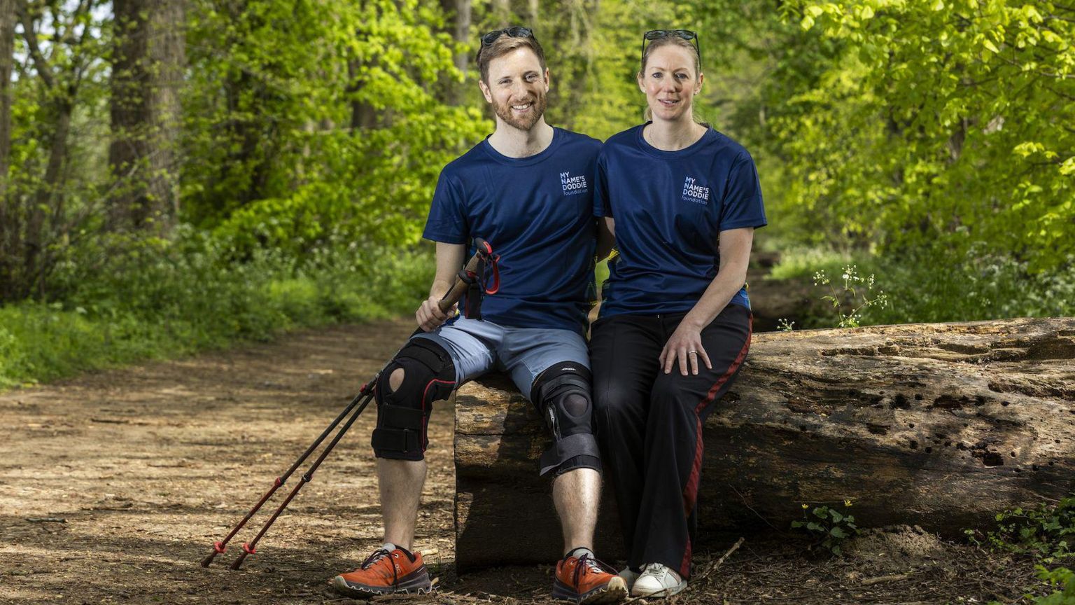 Dr Hames-Brown and his wife, Kate, sitting on a log in a forest
