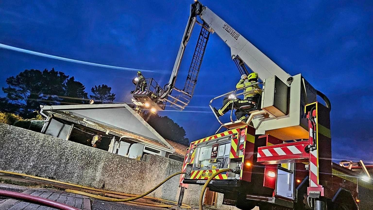 An aerial ladder platform carrying a firefighter who is helping tackle a blaze at a bungalow