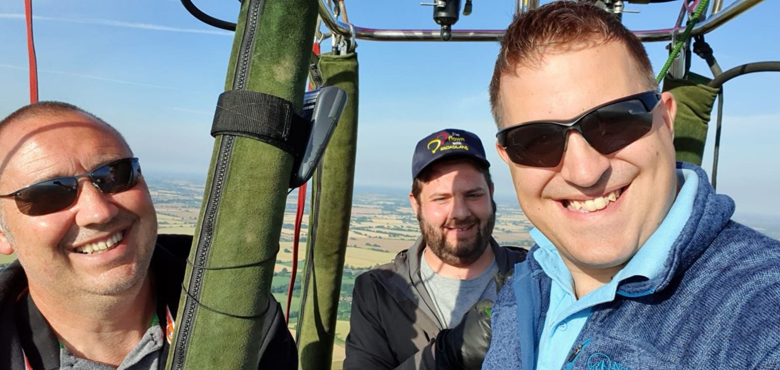 Jon London with two other males smiling at the camera, in a hot air balloon