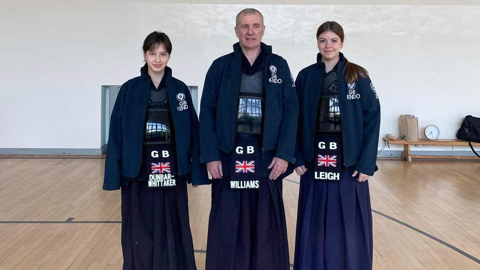 Keira (left), Graham (centre) and Chloe (right) smiling while wearing their Team GB Kendo uniform.