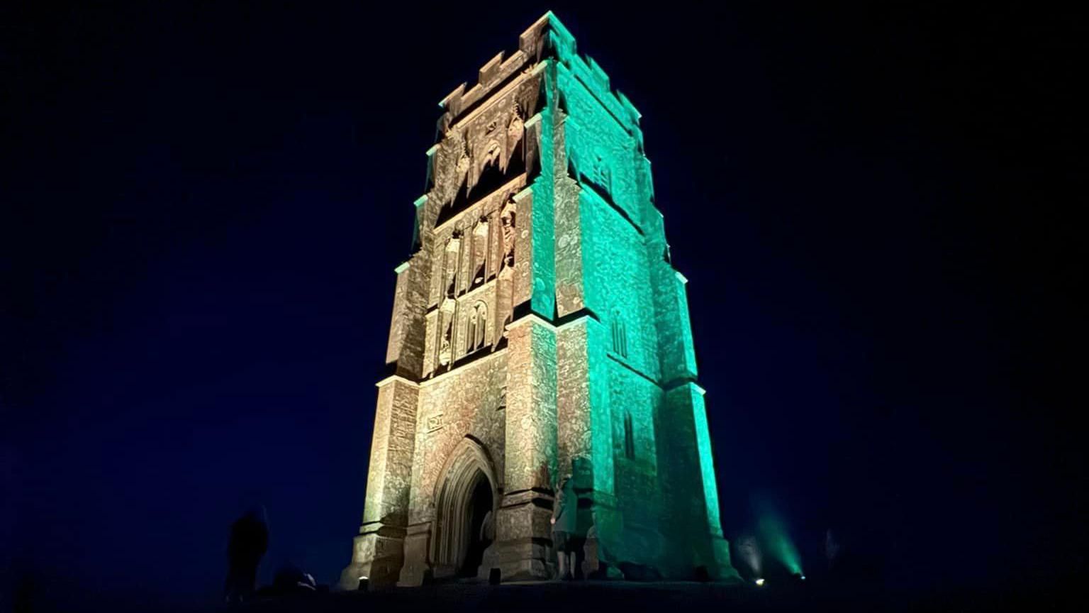 The solitary church tower of Glastonbury Tor lit up green at night