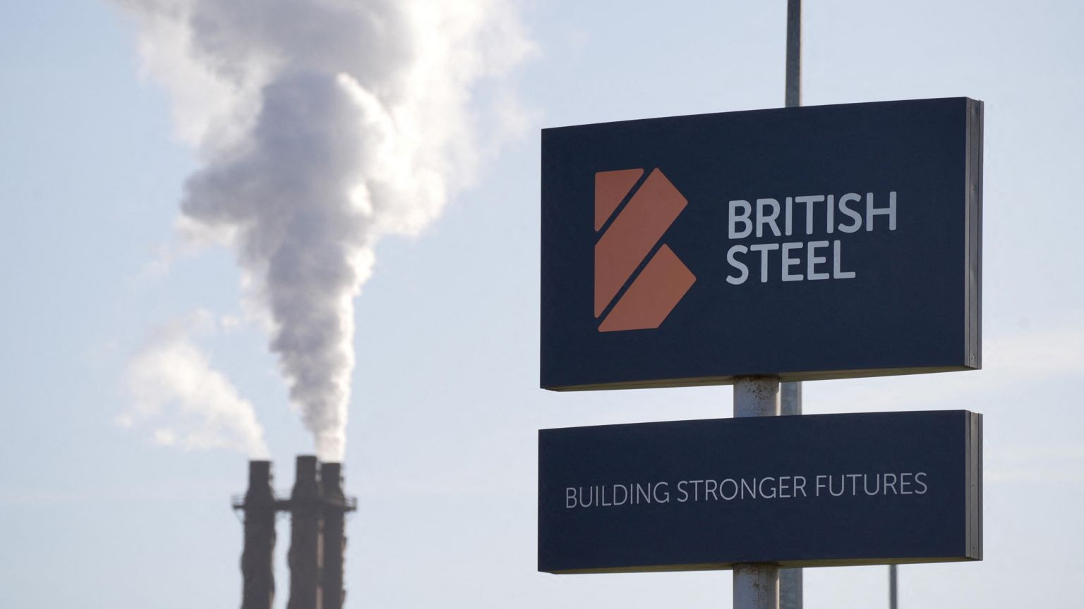 英国钢铁位于英格兰斯肯索普厂区入口的公司标志，背景是在冒烟的烟囱（31/3/2025）