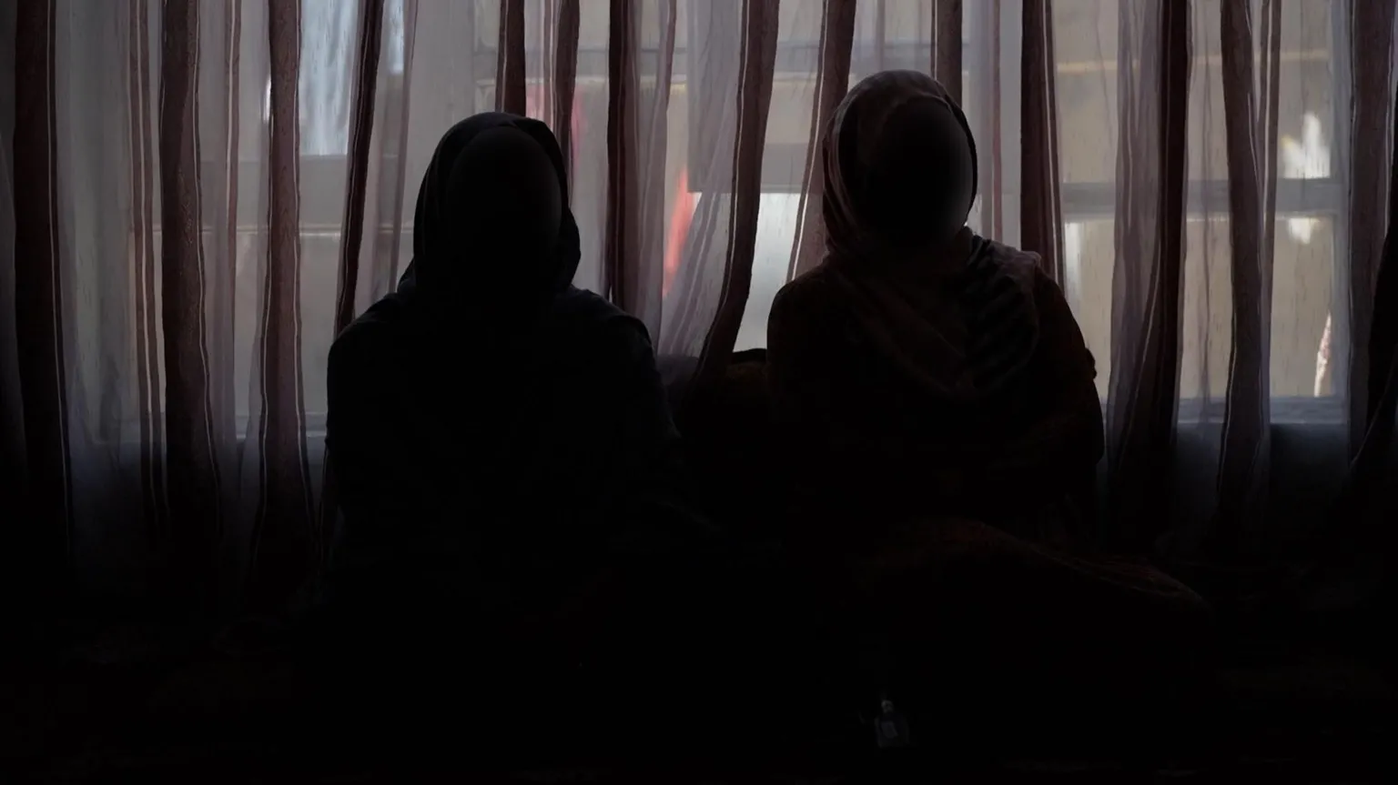 BBC/Imogen Anderson Two women sit in the dark wearing hijabs and face masks to protect their identity