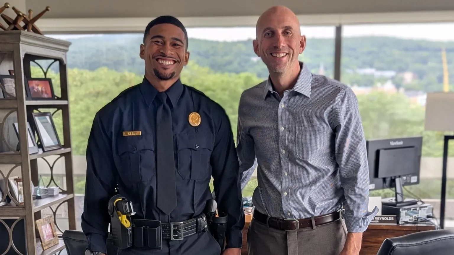 Bethlehem Police Department Sean Reifel and Mayor Reynolds seen smiling and posing for a photo in an office. Sean is wearing an officer's uniform. The mayor is wearing a button-down shirt and slacks.