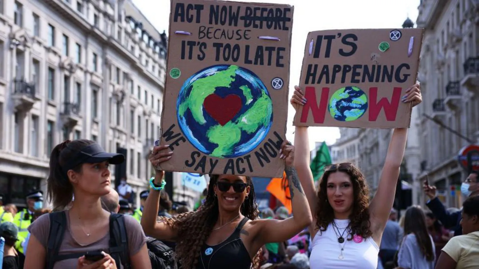 The image shows environmental protesters on a city street holding handmade signs. One sign reads 