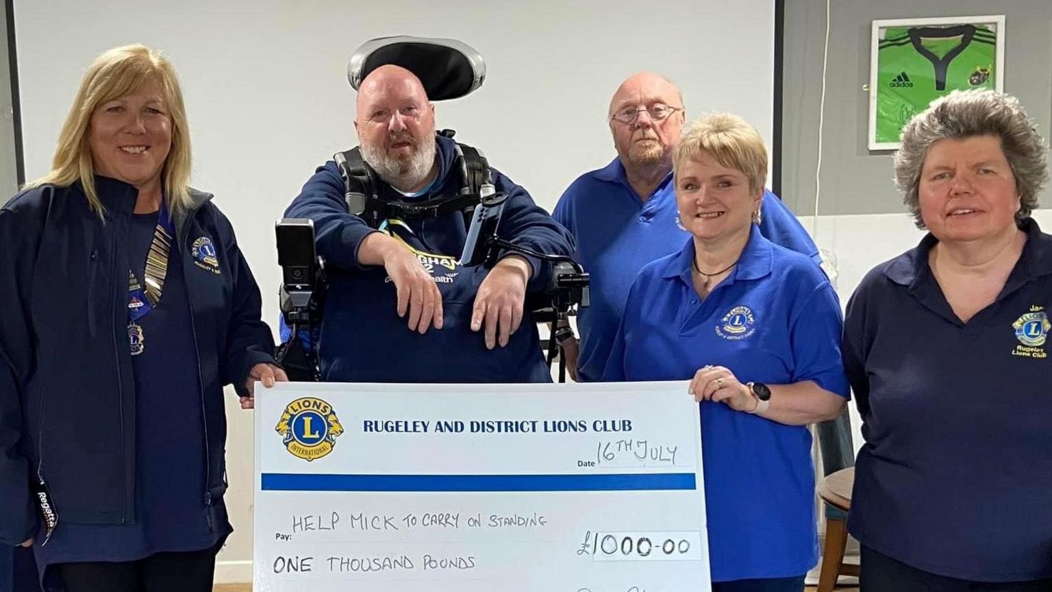 Mick Lloyd pictured with people from the Rugeley and District Lions Club who are holding a big cheque which says £1,000 on it. 