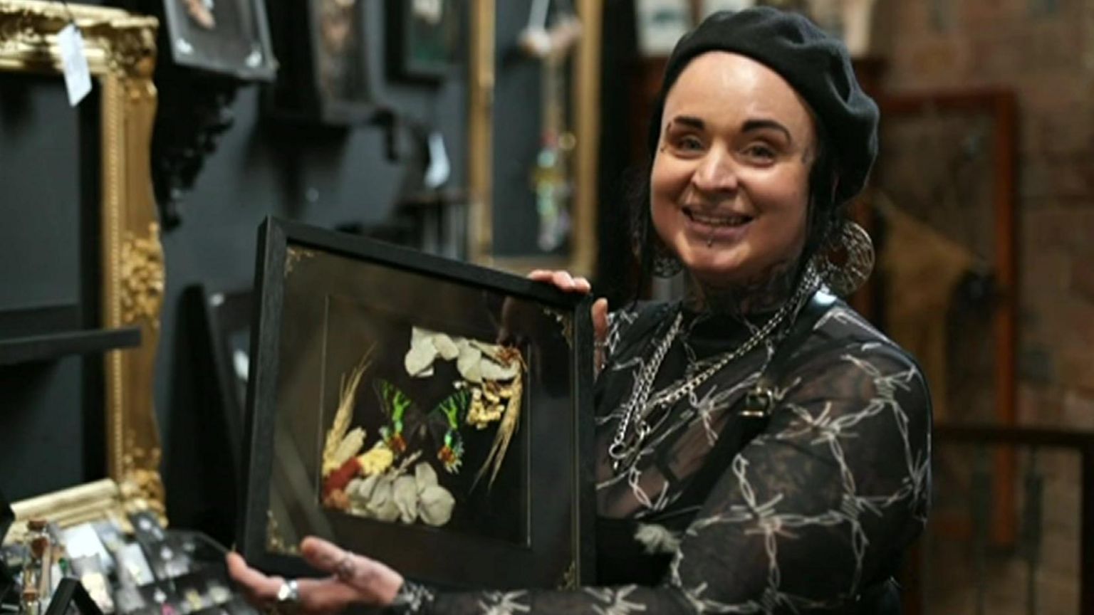 Carrie-Anne Moore, who runs alternative store Broken Bonds in Digbeth, smiling and holding up a framed picture of a butterfly