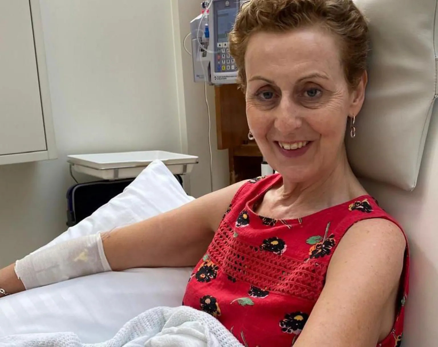 Patricia Hill Patricia sitting in a reclining medical chair in a clinical setting wearing a sleeveless red top