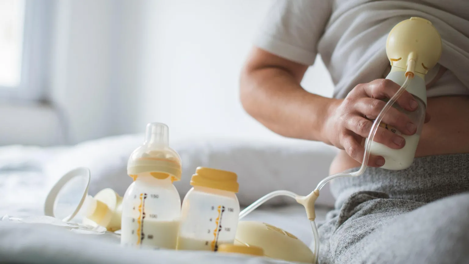 Getty Images A woman uses a breast pump to express milk, with bottles of milk on the bed beside her