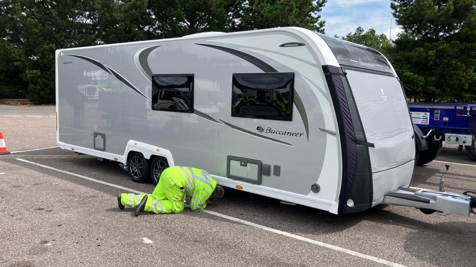 A DVSA staff member in high-vis clothing inspecting the underside of a silver caravan