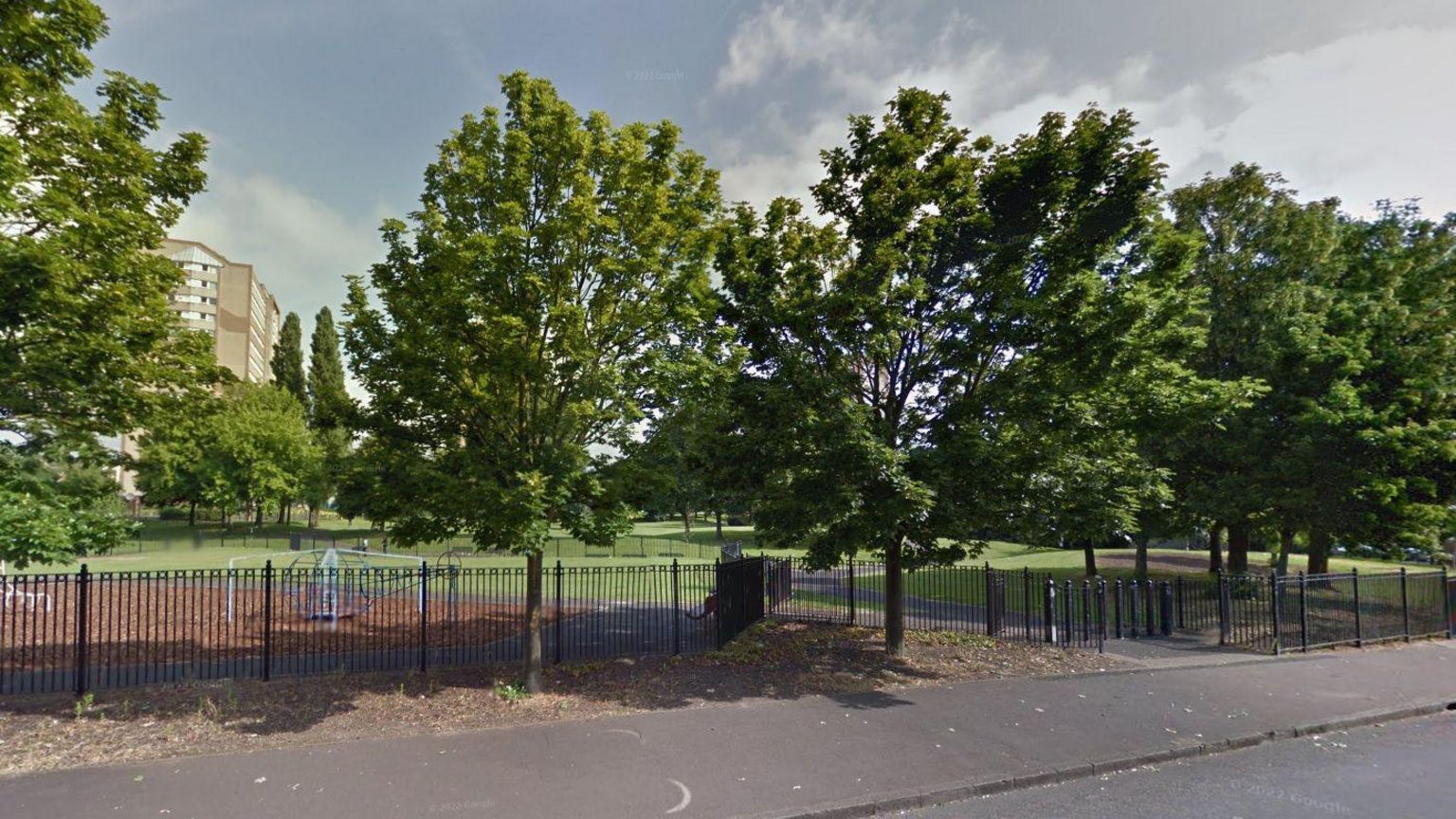 A view of Bloomsbury Park showing trees, grass and a play area behind a fence