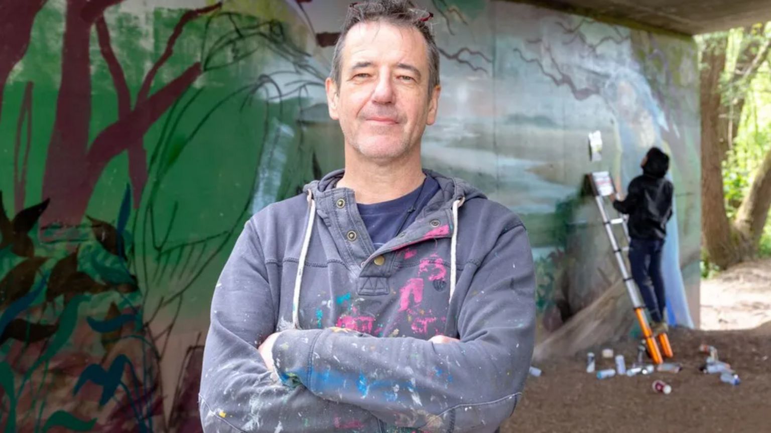 Andy Davies standing inside a subway with someone painting in the background