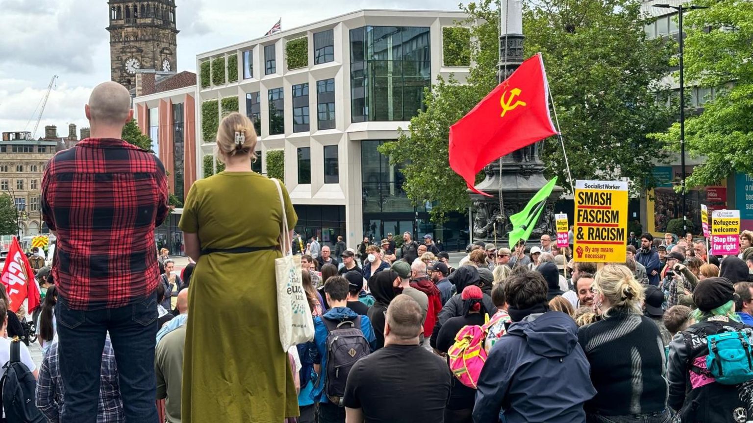 A large group of People in Sheffield gather. One is holding up a yellow sign with the words 'smash fascism and racism',