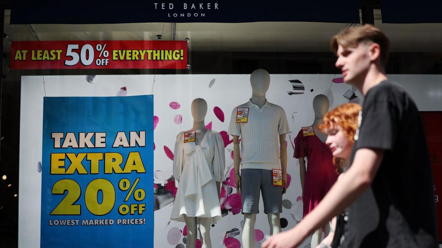 Couple walking past a Ted Baker store with clearance sale signs in the window