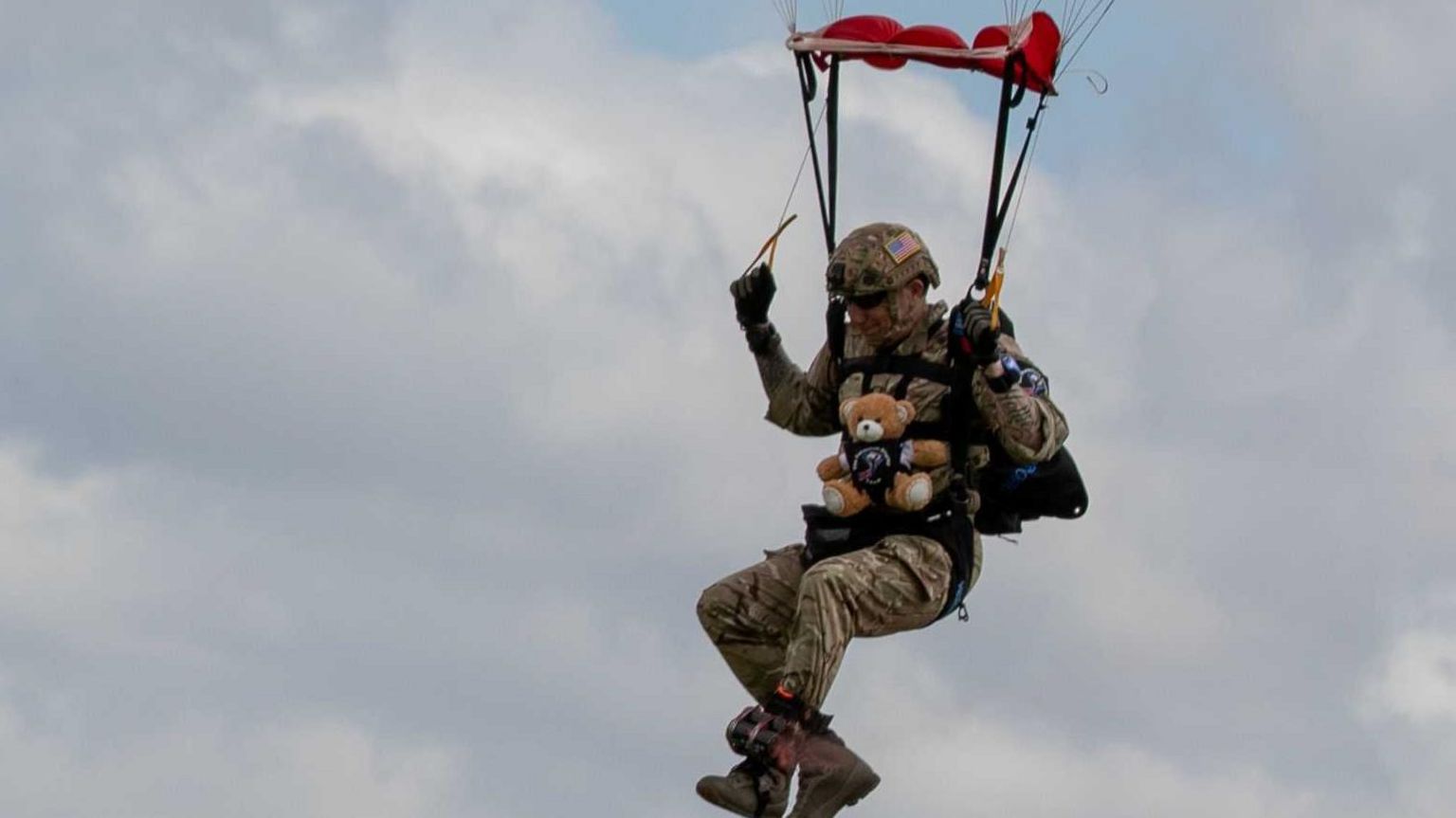 Army member skydiving with toy teddy bear