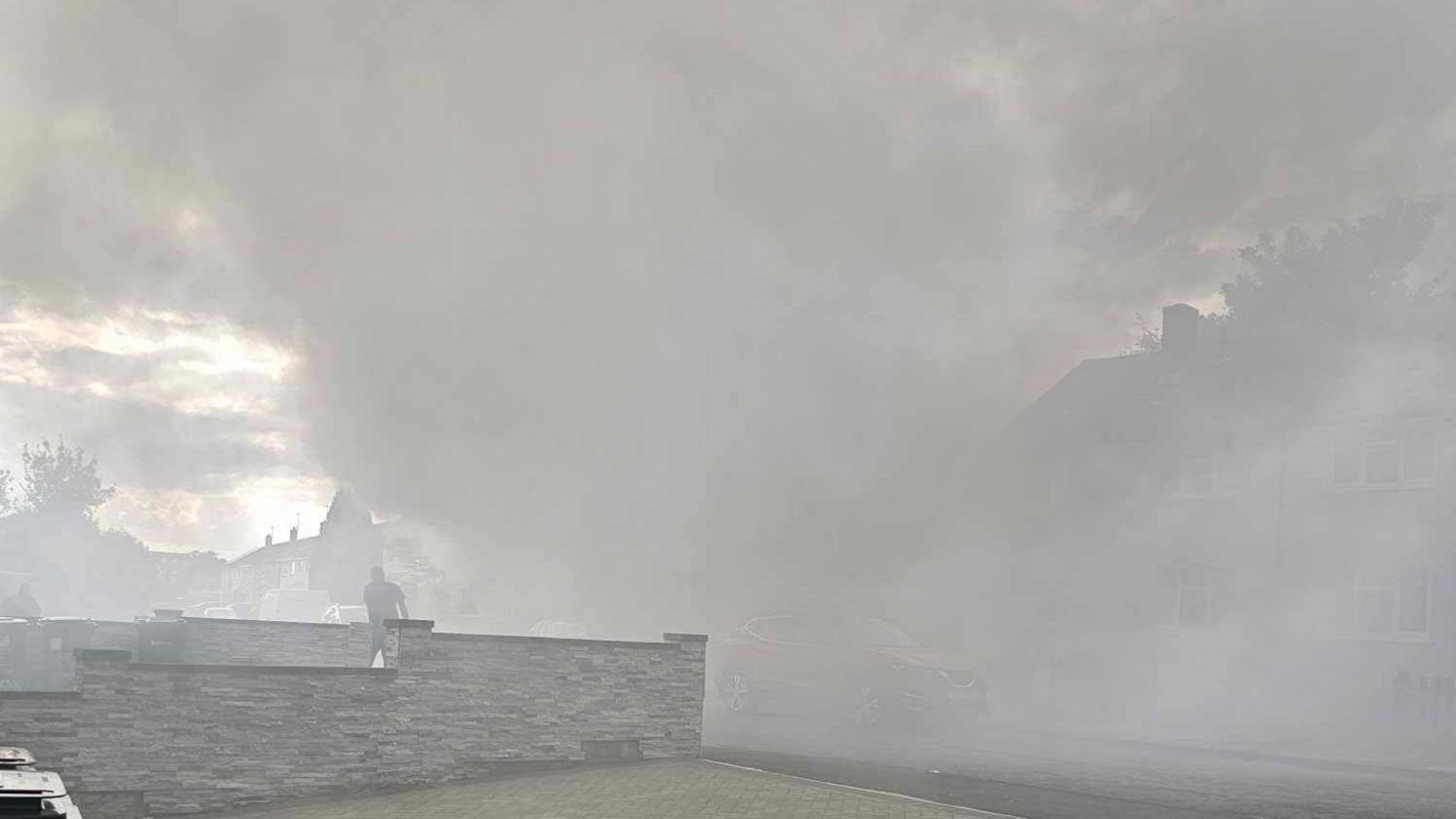 Thick smoke in a road with the faint outline of houses in the background. 