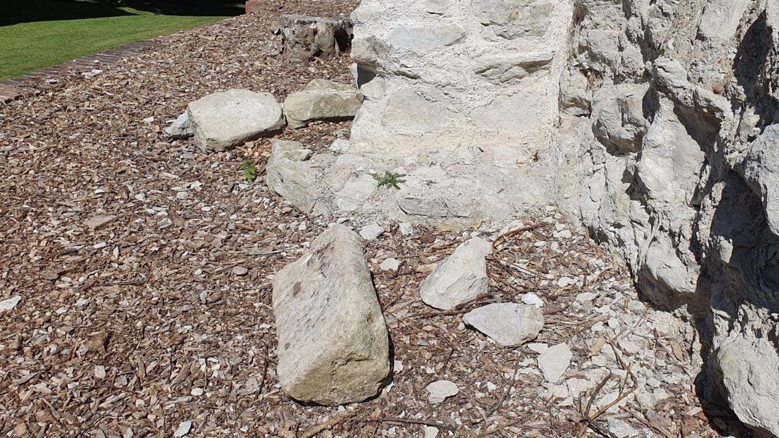 A large grey stone brick is on the floor in front of a castle wall, with other smashed pieces of stone around it.