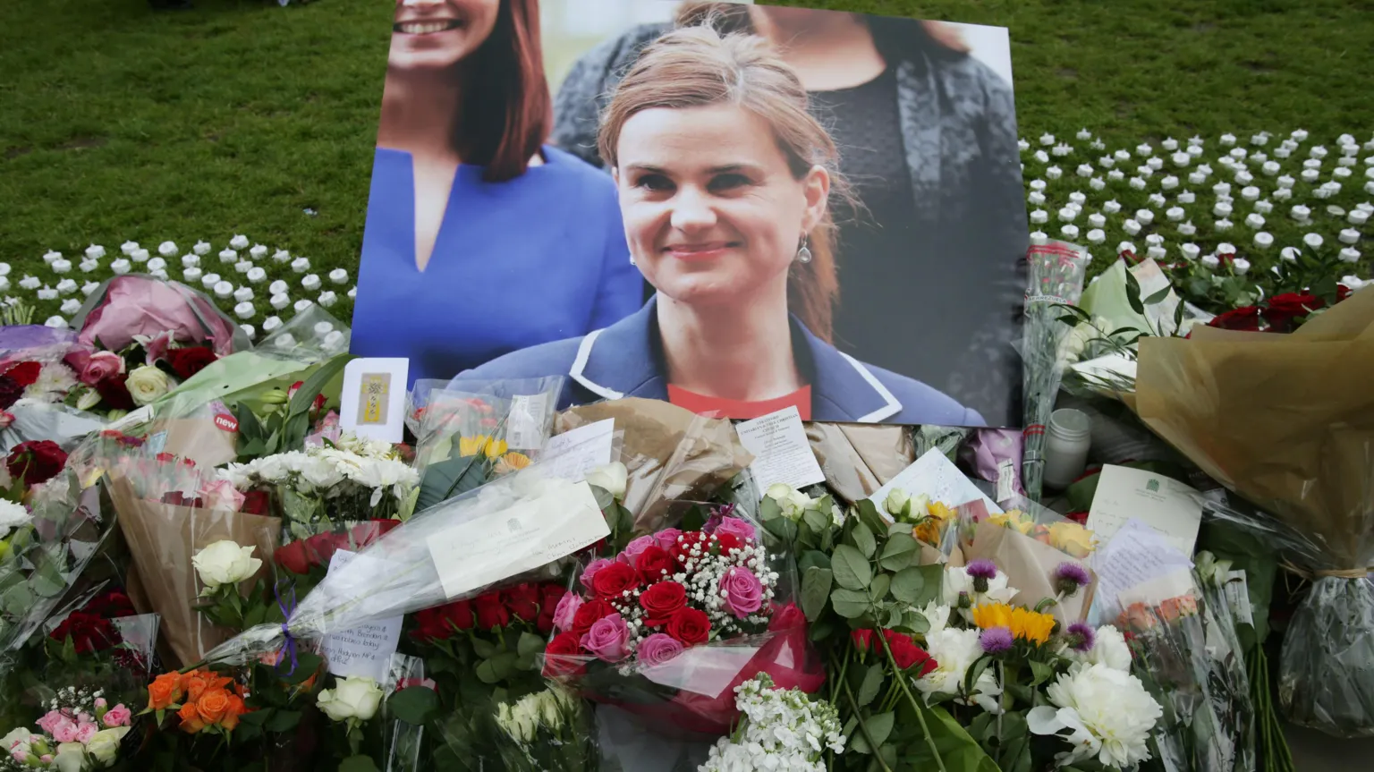 PA Media Image shows a picture of former MP Jo Cox surrounded by bouquets of flowers laid out on grass.