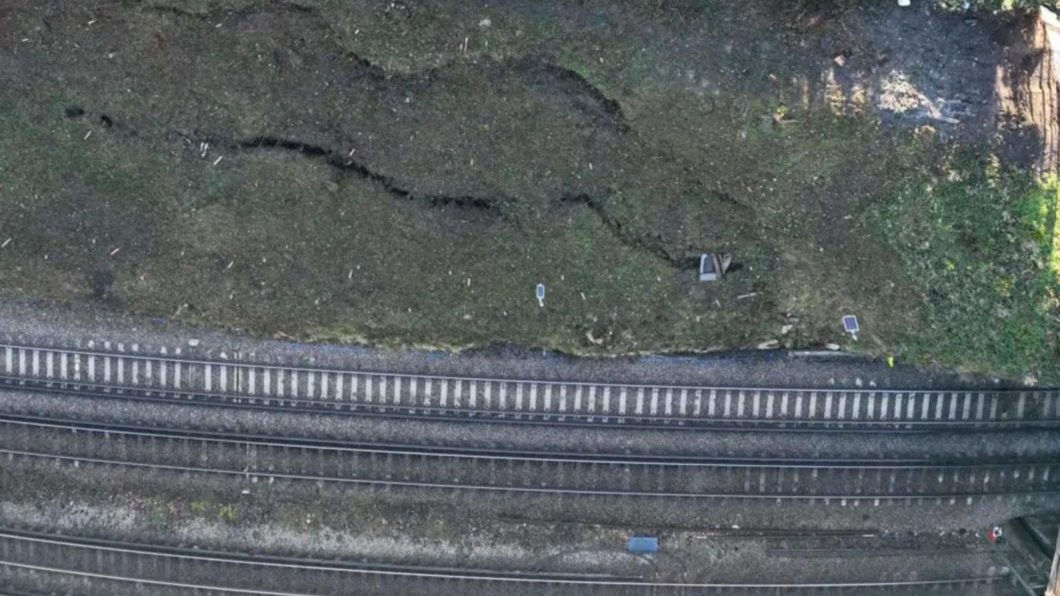 Aerial shot of large cracks in the ground besides a railway track