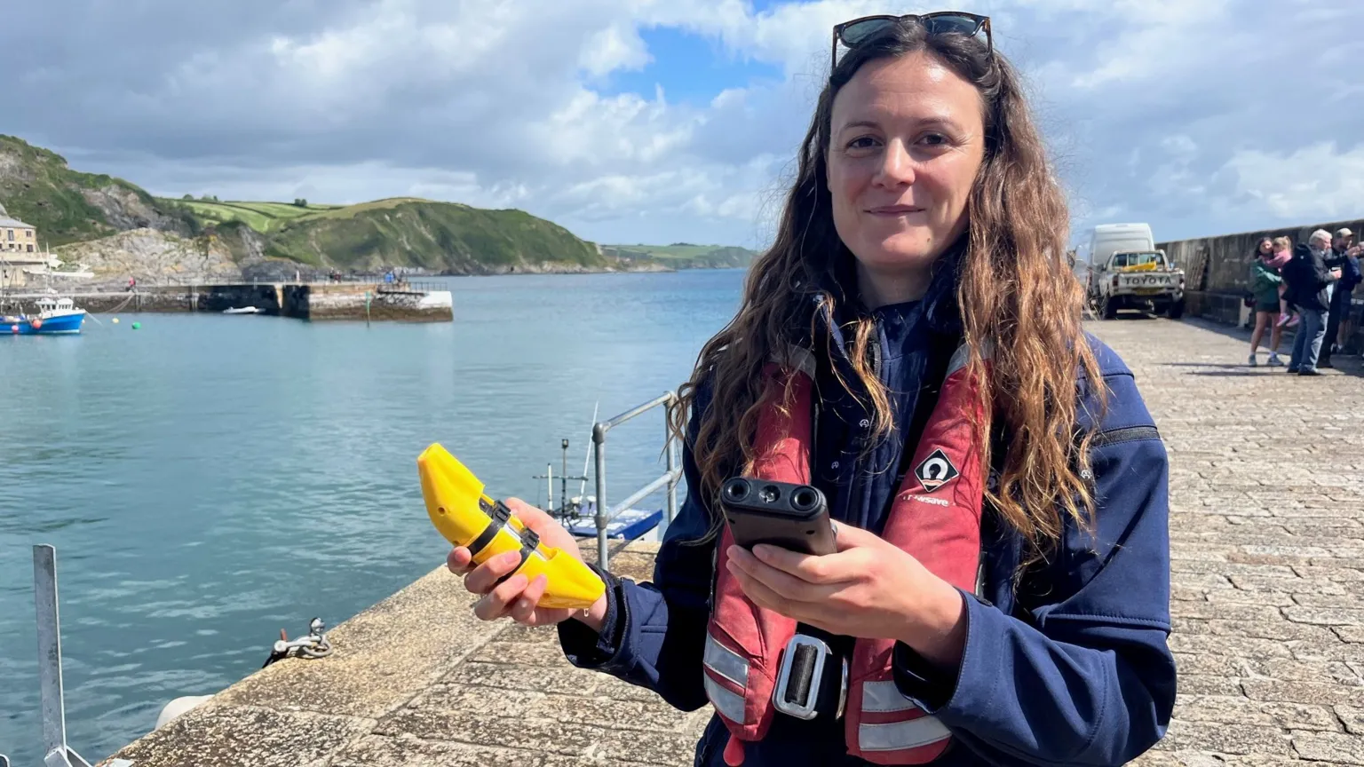 Alessandra Bielli stands on a harbour holding a pinger device to deter dolphins and porpoises, which resembles a banana.