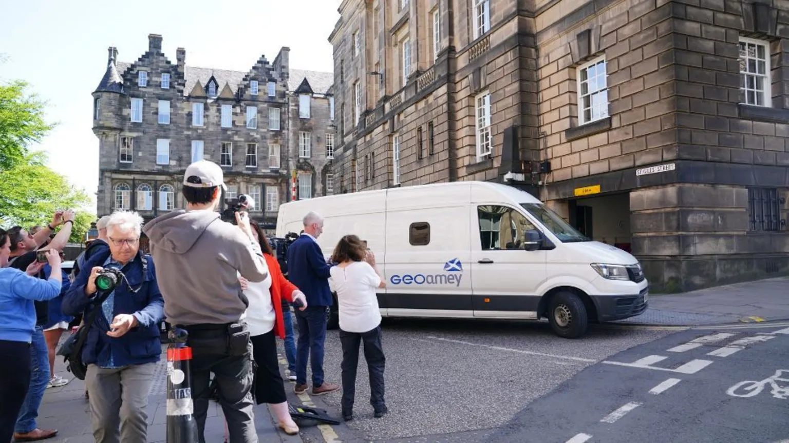 PA Media A white van outside a stone building, with photographers crowding around it