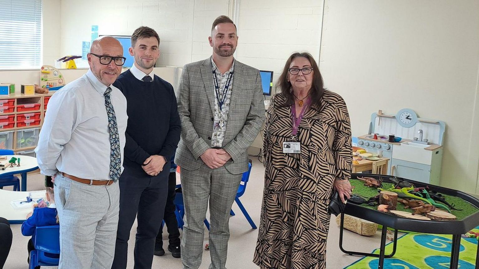 Three men and a woman, all smartly dressed, stand in a new special educational needs classroom at Dorchester Primary School in Hull. The bright, lightly coloured classroom includes play equipment, storage shelves and children's tables