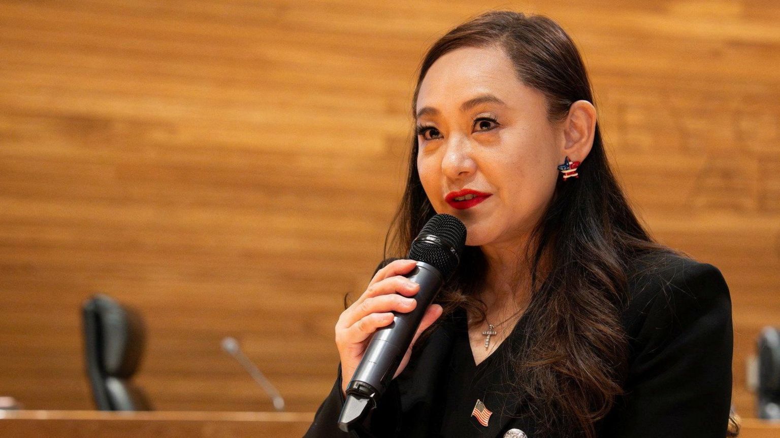 身穿黑色外套,胸前别着美国国旗徽章的王爱琳手持麦克风,在加州阿卡迪亚市政厅发表演说。