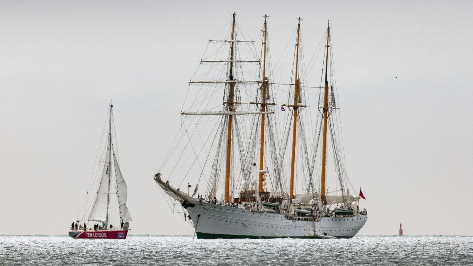 WEDNESDAY - A large white sailing ship with four masts is on the horizon of the Solent, net to it is a smaller red sailing boat with two white sails The sky is a white/grey colour and the sea is glistening in teh sun.