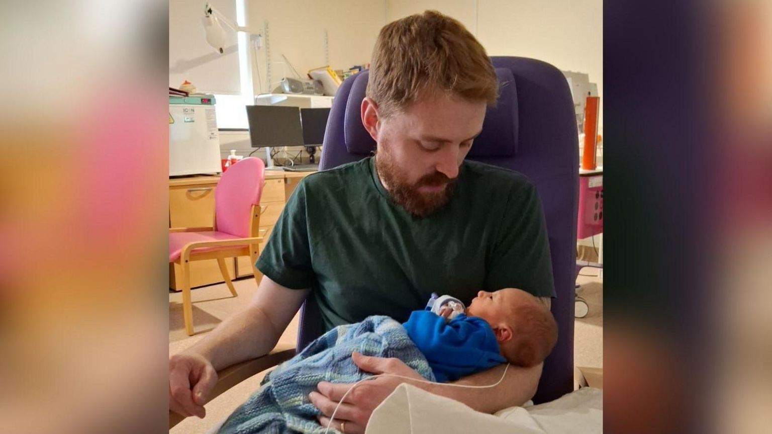 Lewis Daines in a hospital with his baby who is wrapped in a blue woollen blanket