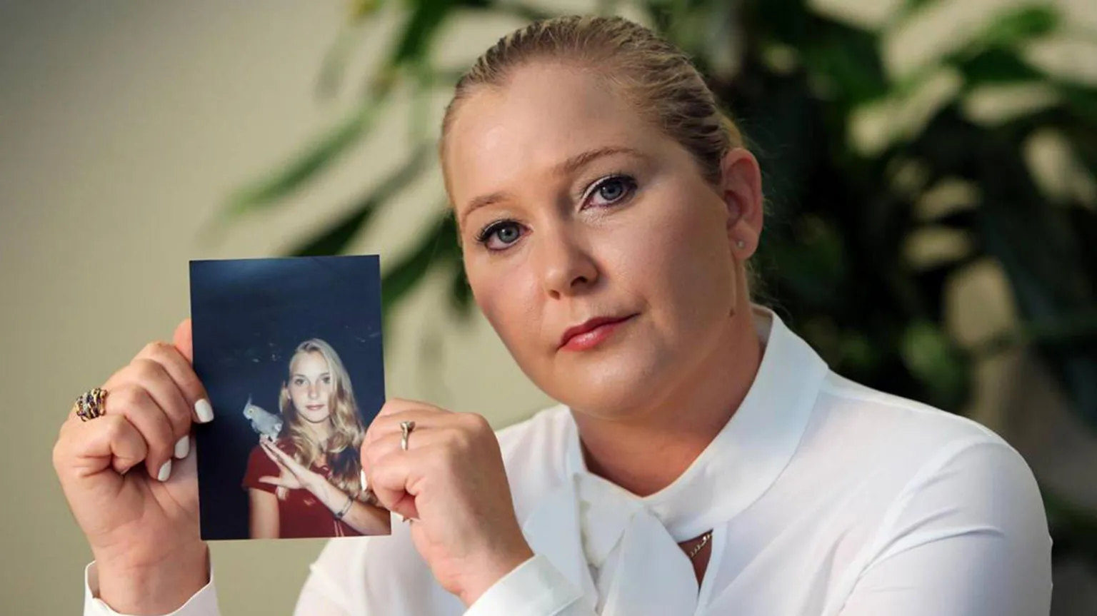Getty Images Virginia Giuffre pictured in November 2022 looking into the camera and holding up a photo of herself as a teenager.