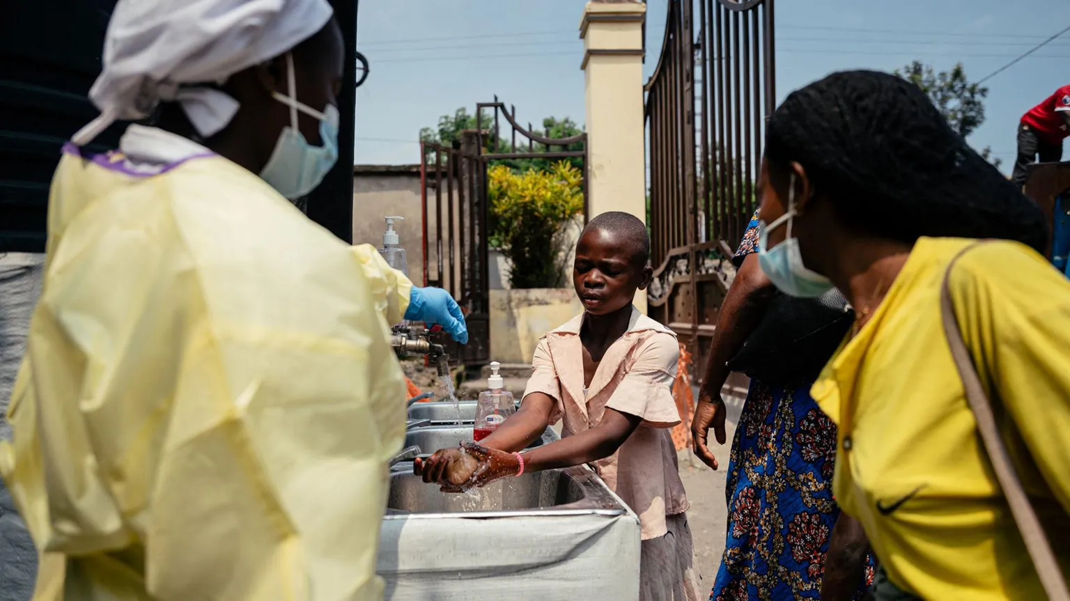 Getty Images A young girl washes her hands at a checkpoint for hand washing and temperature screening for all visitors and patients entering Kyeshero Hospital in Goma, DR Congo on 18 May 2026. Also pictured is a member of medical staff who wears a gown, gloves and face mask, along with another visitor who also wears a face mask.