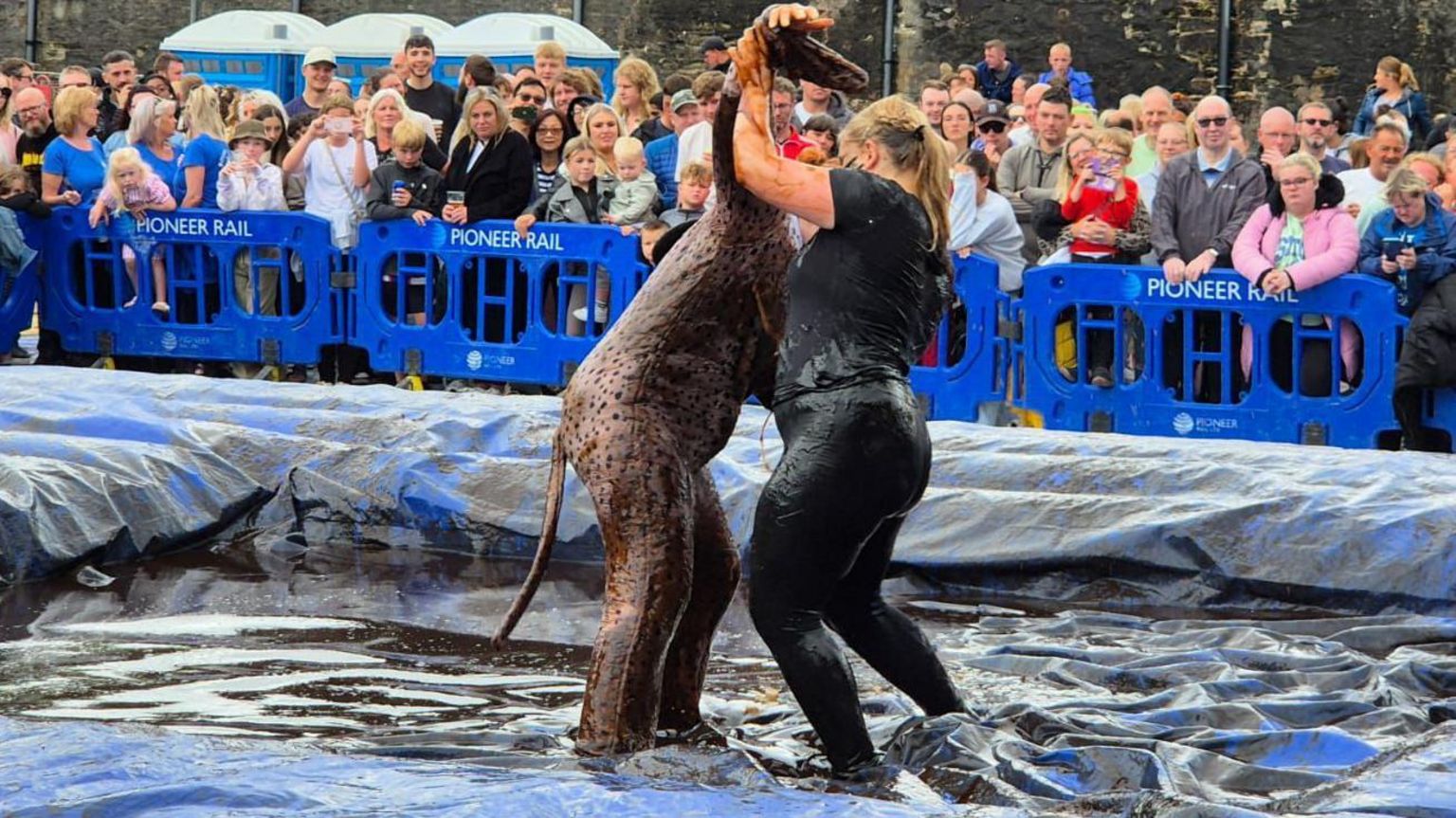 Two women competitors, one dressed as a Dalmatian and the other all in black, in a gravy-soaked ring wrestling