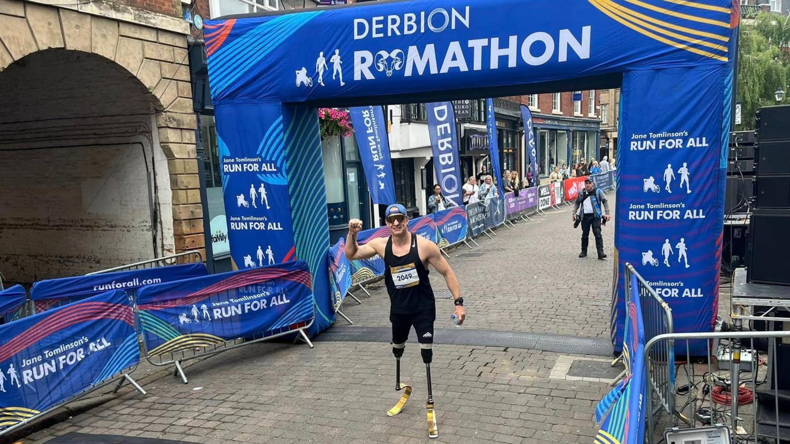 Richard Whitehead at the Ramathon finish line. Around him are blue signs with white writing to show it is the finish line and say "Derby Ramathon"