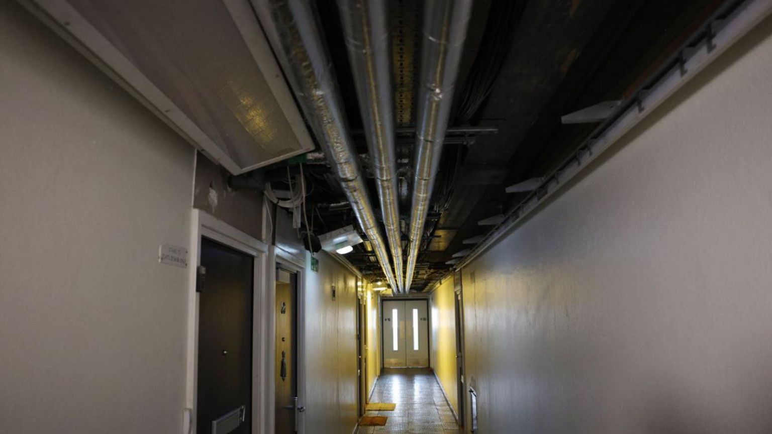 Exposed silver pipework on an uncovered ceiling in a building corridor