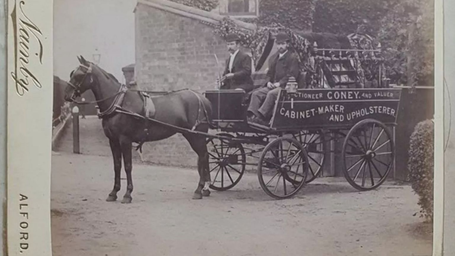 A horse and cart, with two male passengers, in a black and white photo, possibly dating from the late 19th Century. The cart carries the words "Coney, cabinet-maker and upholsterer".