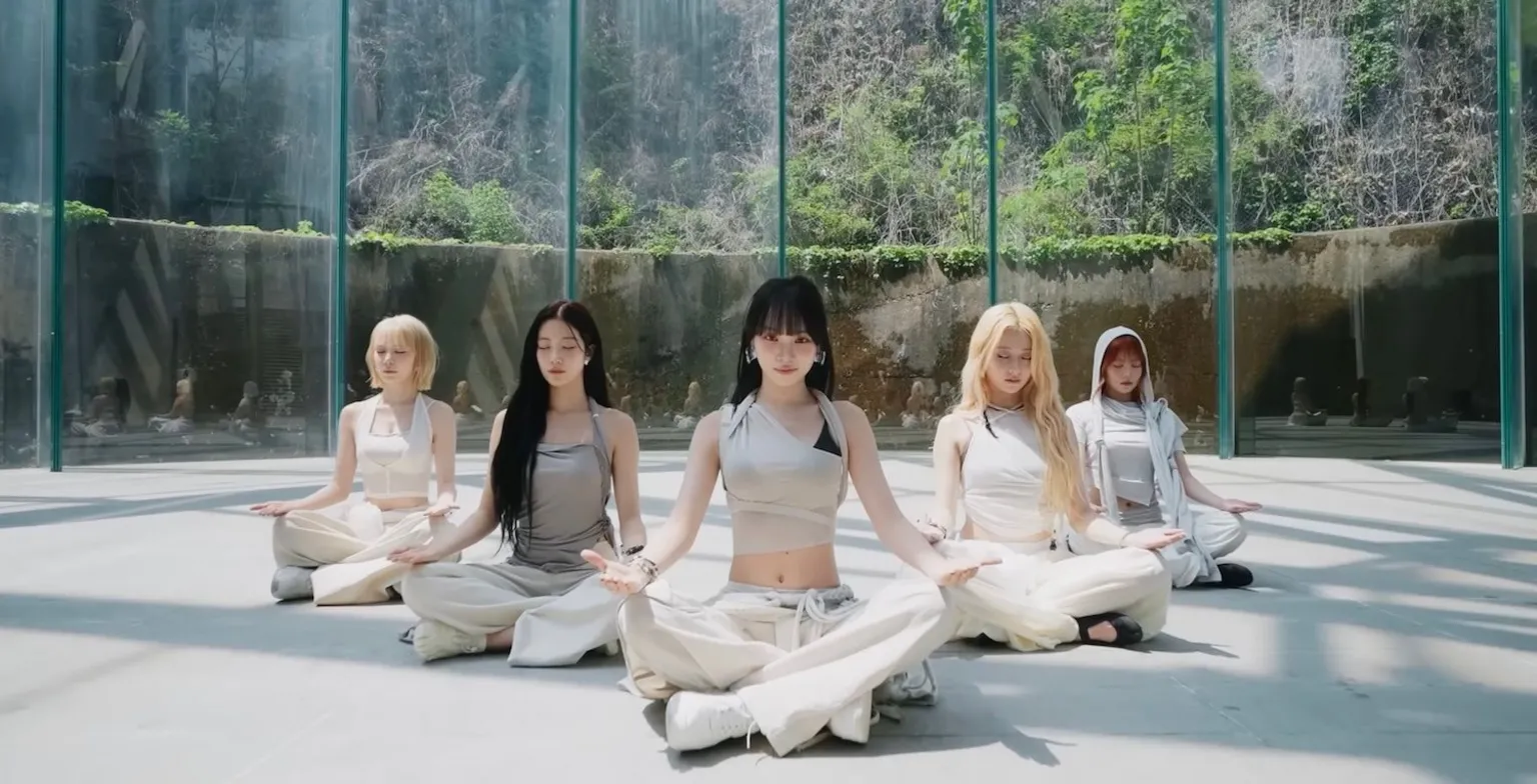 Source Music A still image from the performance video for Le Sserafim's song Boompala shows the band meditating in a plain room, whose windows look out onto a lush, mountainous backdrop