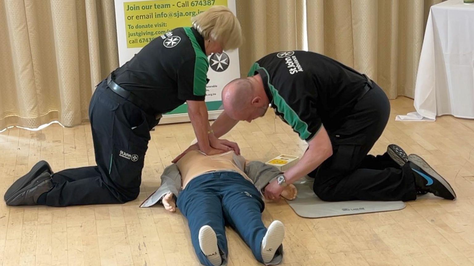 Two volunteers perform CPR and apply a defibrillator to a dummy 
