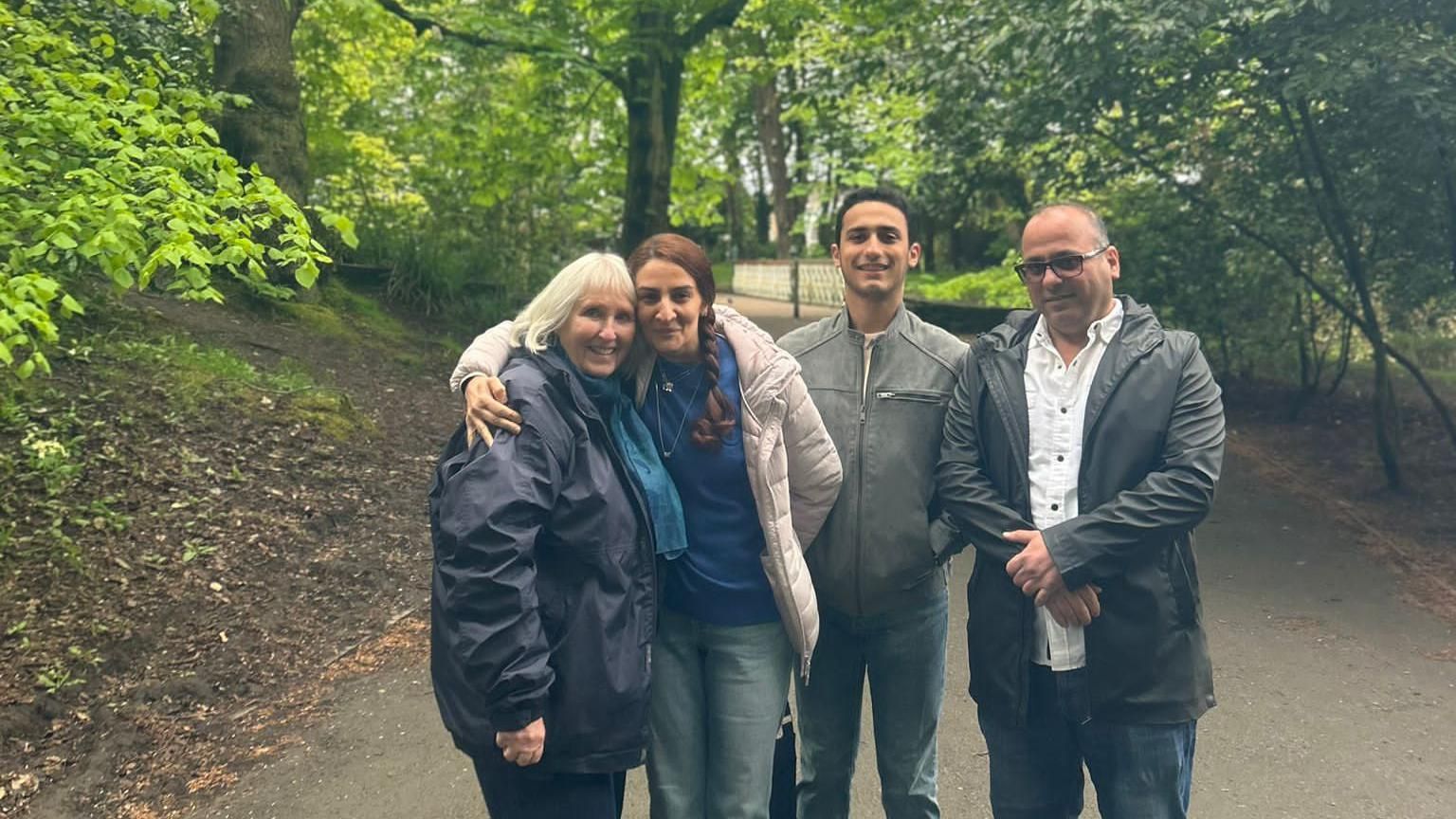 Anne Murray standing with Lara, Azad and their son Darya in a park. Lara is hugging Anne.